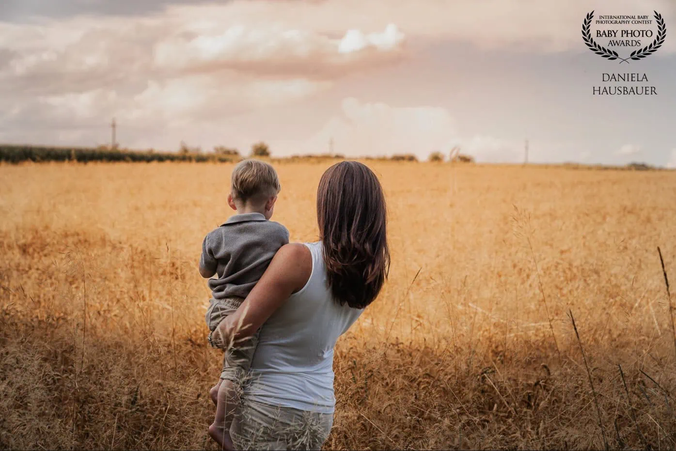 familienfotografin-pischelsdorf-mama-mit-Sohn-im-arm-beim-sonnenuntergang-in-einem-weizenfeld