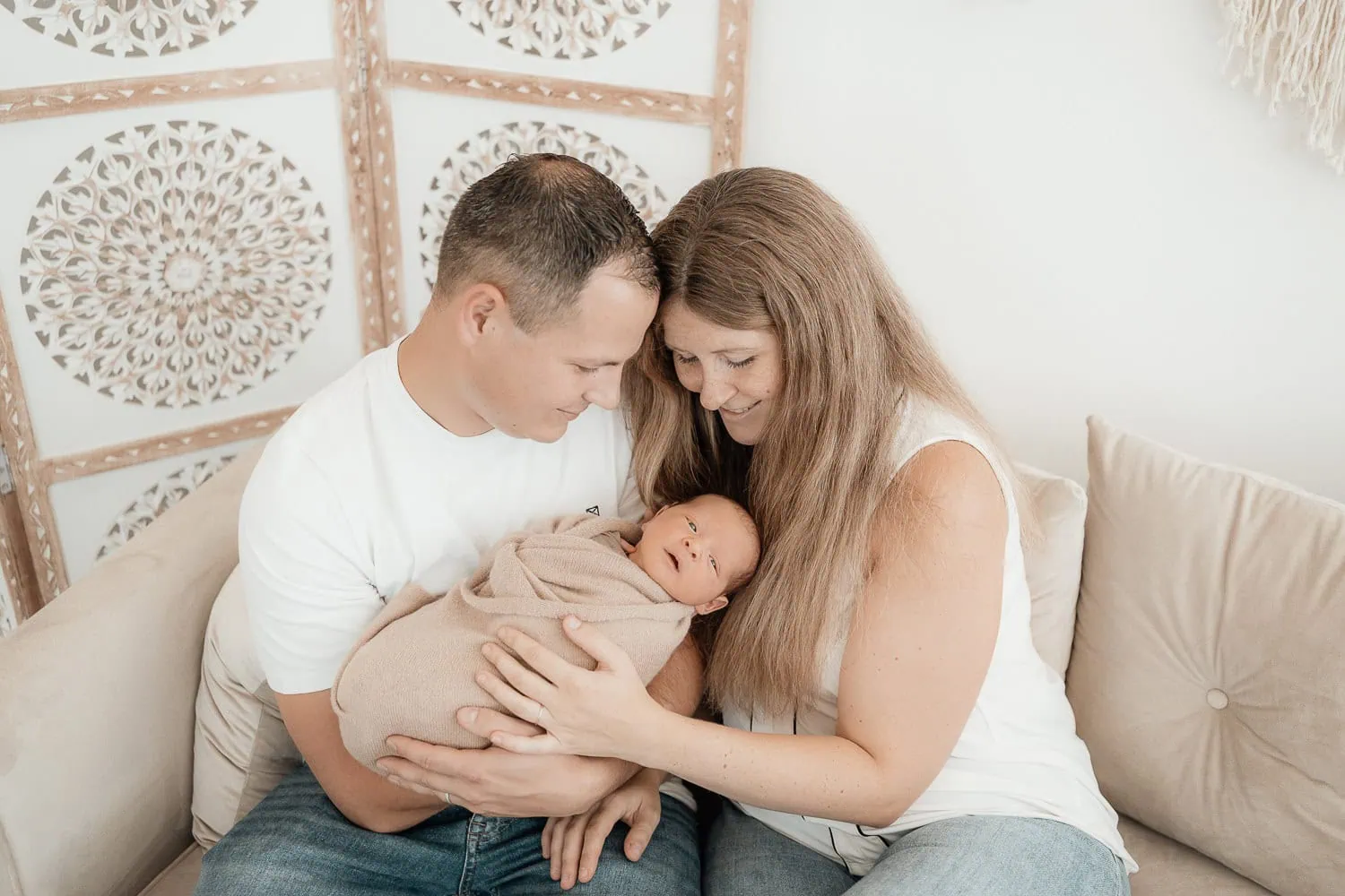 newbornfotografin-pischelsoorf-eltern-sitzen-am-sofa-und-schauen-ihren-sohn-an
